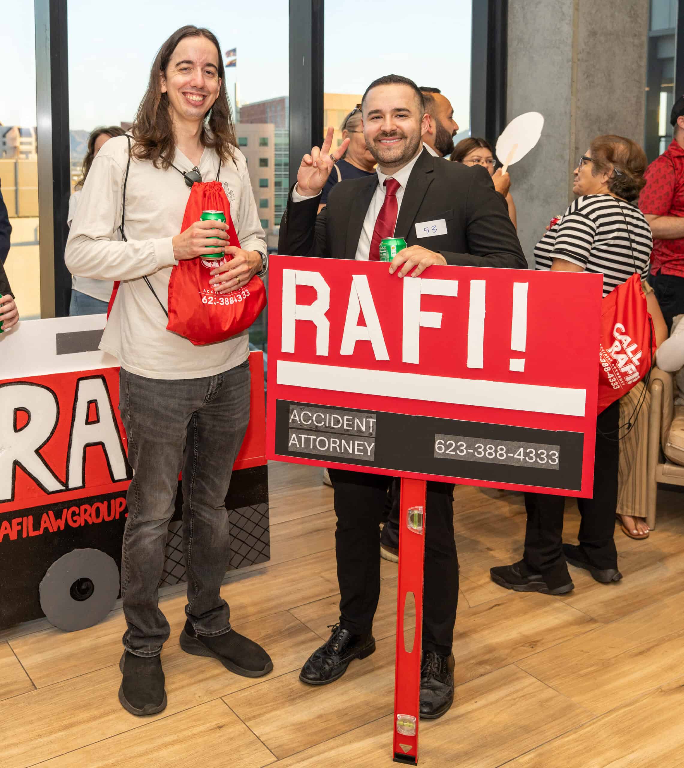 Two people at a Greater Phoenix Chamber event, one holding a red bag and the other holding a sign for Brandon Rafi, Arizona accident attorney.